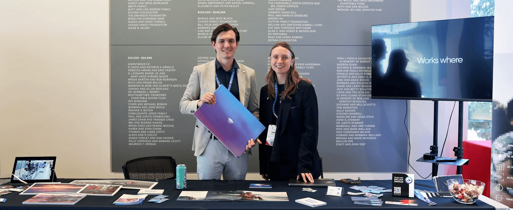 Viesus team at their booth during the Visual 1st conference, showcasing print samples and image enhancement results.